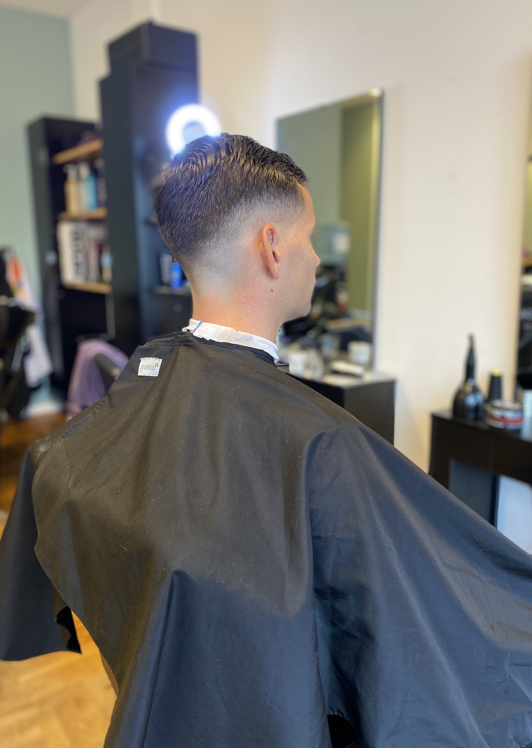 Een strak geknipte fade, gezien vanaf de achterkant in de salon