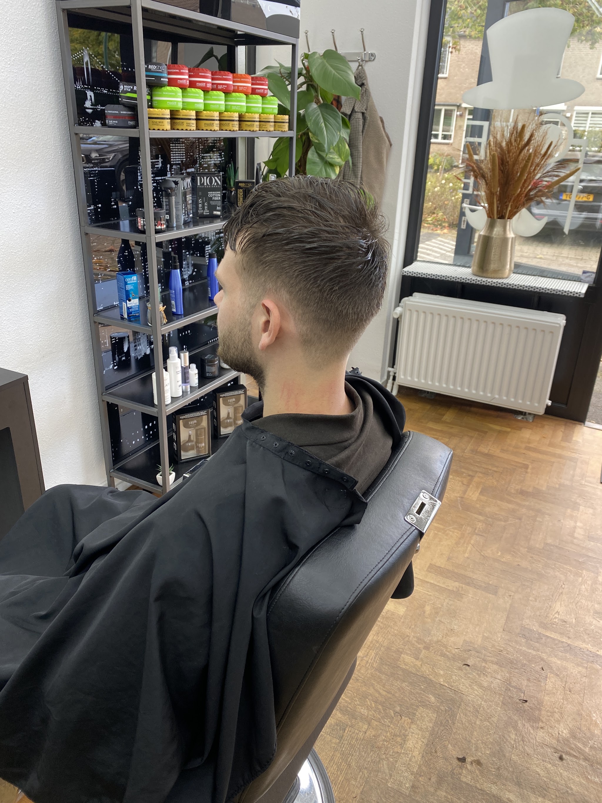 Een klant in de kappersstoel na het knippen, met de productkast op de achtergrond